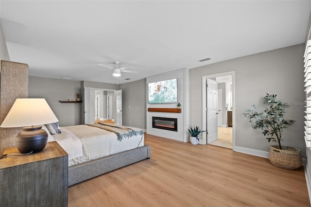 bedroom featuring baseboards, light wood-style flooring, a fireplace, ceiling fan, and connected bathroom