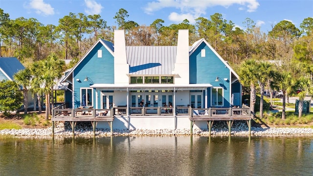 back of house with a deck with water view, a standing seam roof, a chimney, french doors, and metal roof