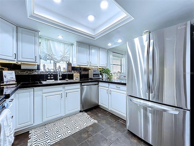 kitchen with a sink, dark countertops, white cabinetry, stainless steel appliances, and a raised ceiling