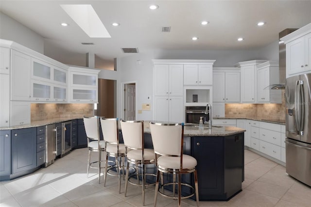 kitchen featuring visible vents, a center island with sink, a sink, white cabinetry, and stainless steel appliances