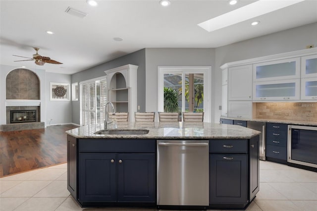 kitchen with a sink, stainless steel dishwasher, open floor plan, light tile patterned floors, and a tile fireplace