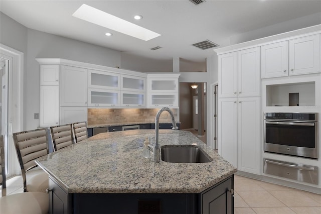 kitchen featuring a warming drawer, visible vents, a center island with sink, a sink, and stainless steel oven