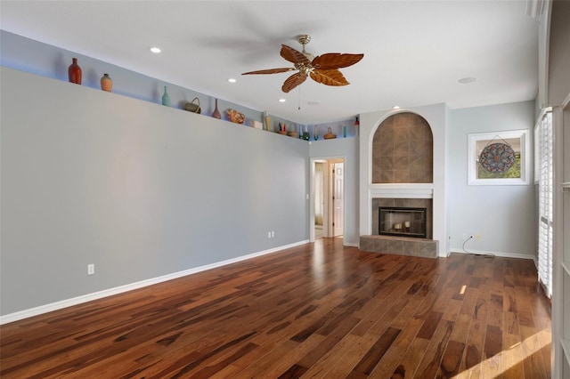 unfurnished living room with baseboards, ceiling fan, a tiled fireplace, and hardwood / wood-style flooring