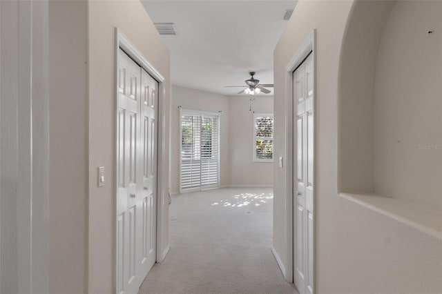 hall with visible vents, light carpet, and baseboards