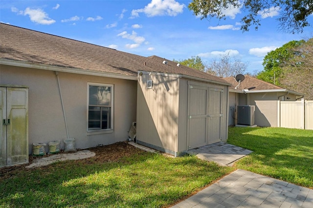 exterior space featuring cooling unit, a lawn, a shingled roof, and fence