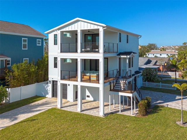 rear view of house featuring a balcony, fence, decorative driveway, a lawn, and board and batten siding