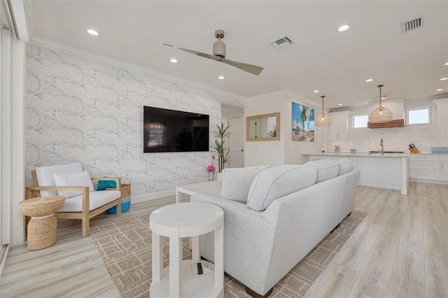 living area with light wood-type flooring, visible vents, recessed lighting, crown molding, and wallpapered walls