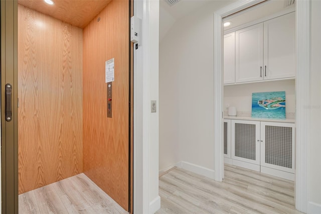 hallway featuring recessed lighting, baseboards, elevator, and light wood finished floors