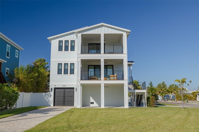 beach home featuring a front lawn, fence, board and batten siding, concrete driveway, and a balcony