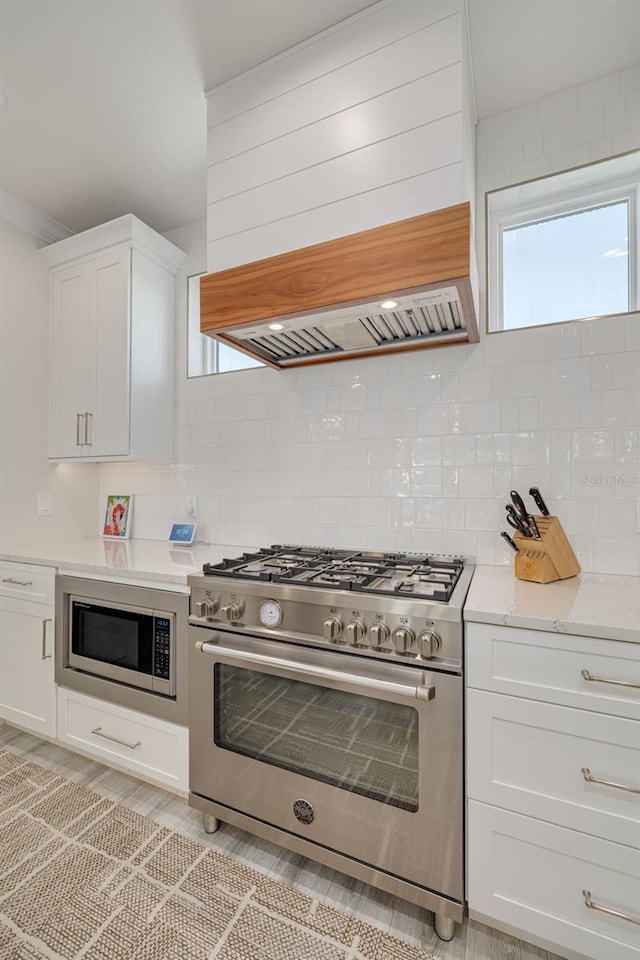 kitchen with backsplash, light stone countertops, custom range hood, stainless steel appliances, and white cabinetry