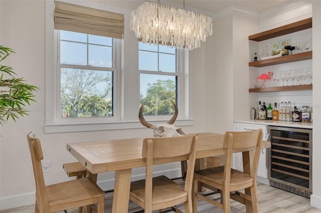 dining space with light wood finished floors, beverage cooler, ornamental molding, a notable chandelier, and a bar