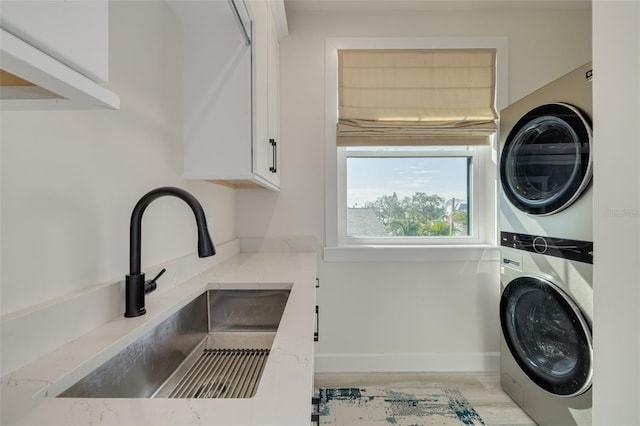 laundry area with light wood finished floors, baseboards, laundry area, stacked washer / drying machine, and a sink