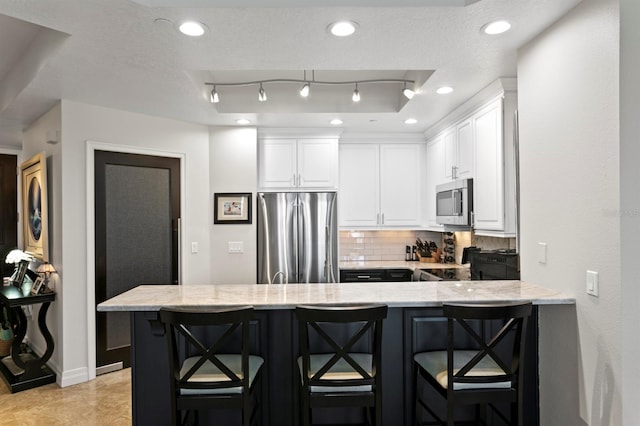 kitchen featuring white cabinetry, light stone counters, tasteful backsplash, and appliances with stainless steel finishes