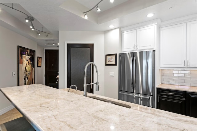 kitchen featuring light stone countertops, decorative backsplash, recessed lighting, freestanding refrigerator, and white cabinetry