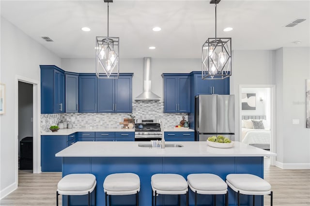 kitchen featuring wall chimney range hood, blue cabinets, a breakfast bar area, and appliances with stainless steel finishes