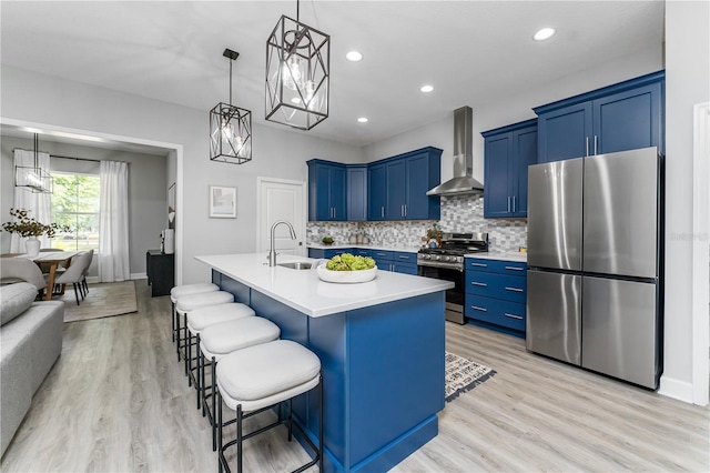 kitchen with a sink, light countertops, blue cabinets, appliances with stainless steel finishes, and wall chimney exhaust hood