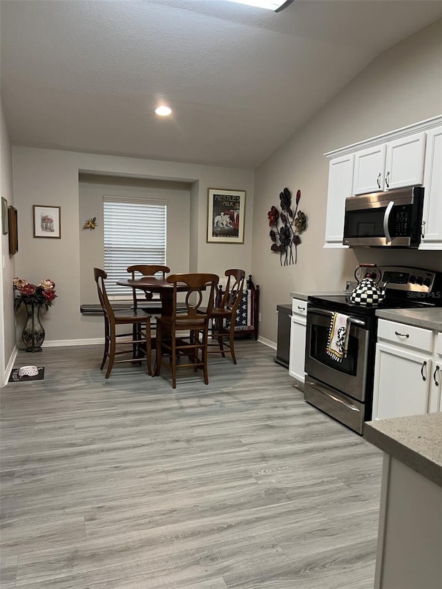 kitchen featuring stainless steel appliances, light wood-style floors, white cabinets, baseboards, and vaulted ceiling