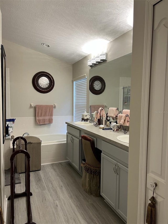 full bath with double vanity, wood finished floors, a bath, a textured ceiling, and a sink