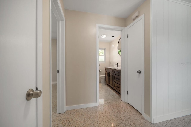 corridor with a sink, baseboards, and light speckled floor