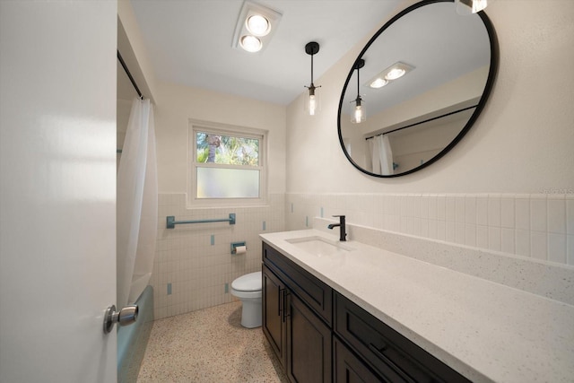 bathroom with a wainscoted wall, toilet, vanity, tile walls, and speckled floor