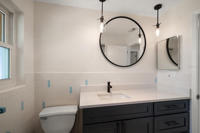 bathroom featuring visible vents, a wainscoted wall, toilet, vanity, and tile walls