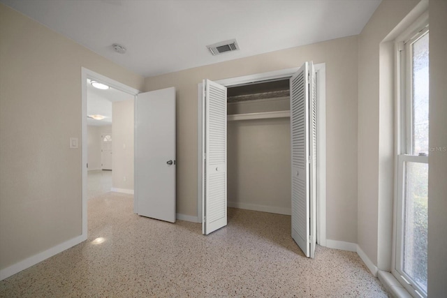 unfurnished bedroom featuring speckled floor, baseboards, a closet, and visible vents