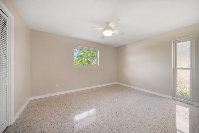 spare room featuring a ceiling fan, speckled floor, and baseboards