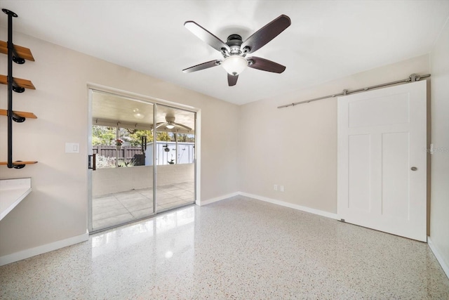 spare room with a ceiling fan, a barn door, baseboards, and speckled floor