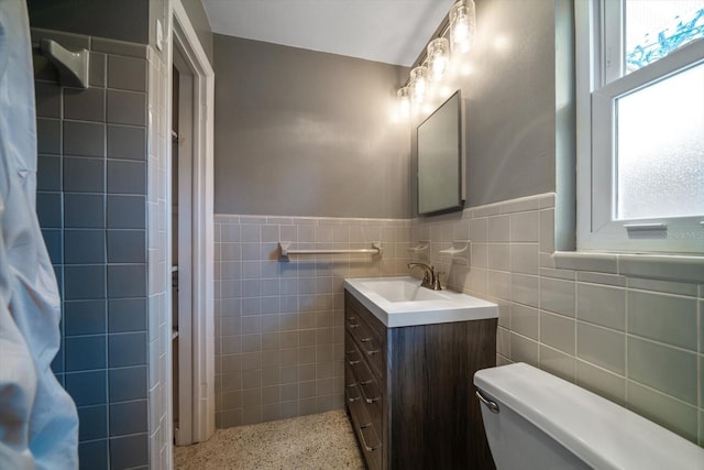 full bathroom with a wainscoted wall, toilet, tile walls, and speckled floor