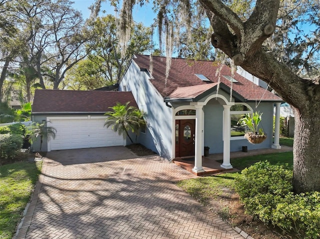 view of front facade with decorative driveway, roof with shingles, an attached garage, and stucco siding