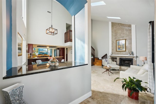 kitchen featuring visible vents, high vaulted ceiling, dark stone counters, a fireplace, and a notable chandelier