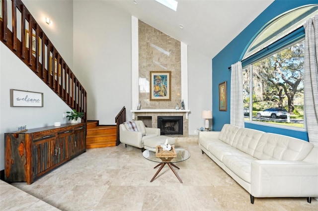 living room with a tiled fireplace, a skylight, high vaulted ceiling, and stairs