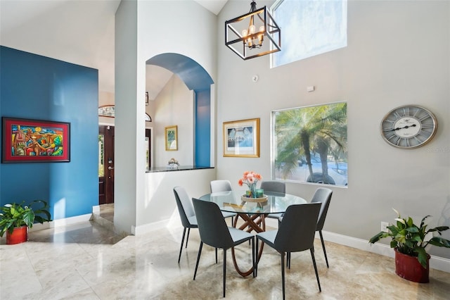 dining space featuring arched walkways, a chandelier, a high ceiling, and baseboards