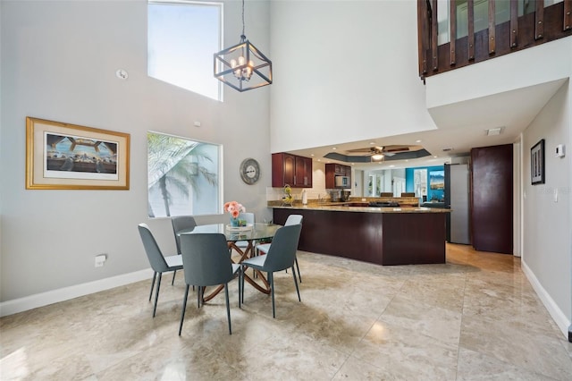 dining space featuring baseboards, a high ceiling, and ceiling fan with notable chandelier