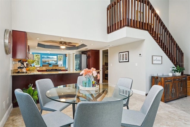 dining room featuring a raised ceiling, a towering ceiling, recessed lighting, baseboards, and ceiling fan