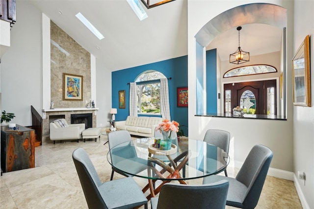 dining area featuring a tiled fireplace, high vaulted ceiling, a skylight, and baseboards