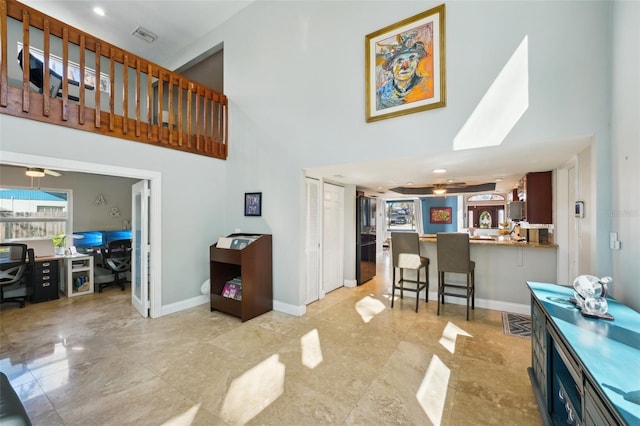 living area with a ceiling fan, visible vents, a towering ceiling, and baseboards