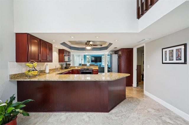 kitchen with light stone countertops, appliances with stainless steel finishes, a peninsula, a raised ceiling, and a sink