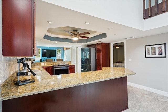 kitchen with stainless steel electric stove, freestanding refrigerator, reddish brown cabinets, a peninsula, and a raised ceiling