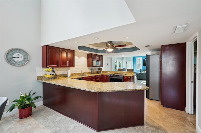 kitchen featuring a ceiling fan, a peninsula, a tray ceiling, appliances with stainless steel finishes, and reddish brown cabinets