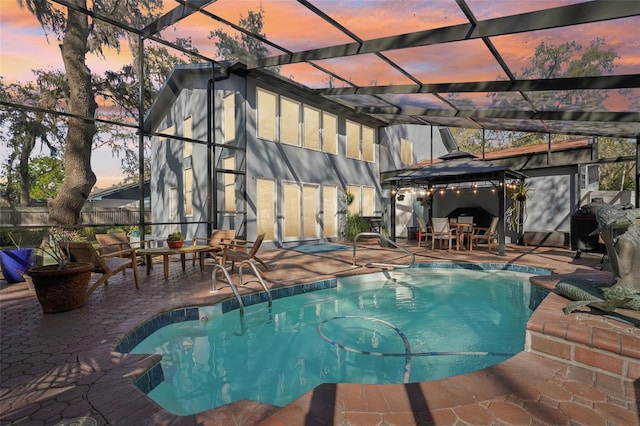 pool at dusk featuring an outdoor pool, a gazebo, a lanai, and a patio area