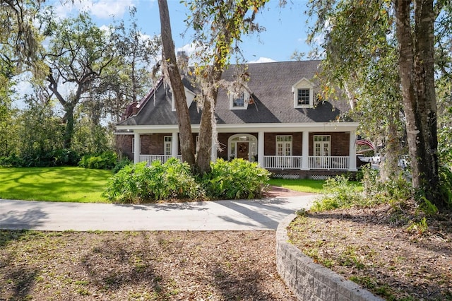 new england style home with brick siding, covered porch, and a front yard