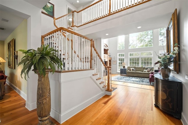 stairway featuring hardwood / wood-style flooring, baseboards, visible vents, and a towering ceiling