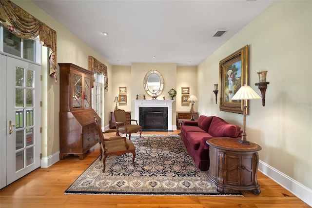 living area with wood finished floors, visible vents, baseboards, a fireplace, and french doors