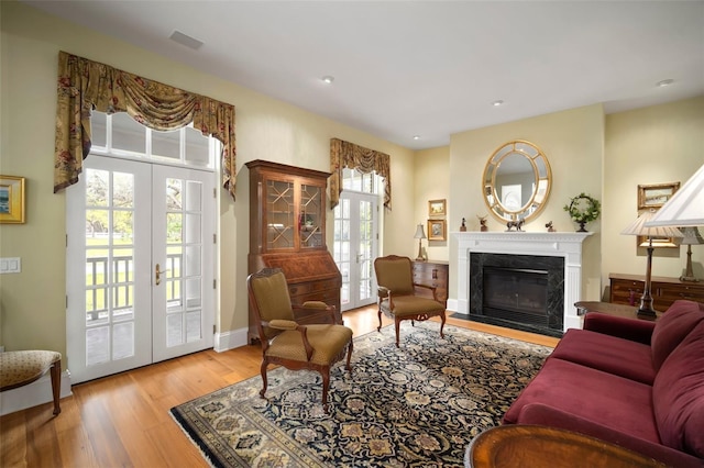 living area featuring french doors, baseboards, light wood-style floors, and a premium fireplace