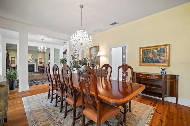 dining room with a glass covered fireplace, visible vents, an inviting chandelier, and wood finished floors