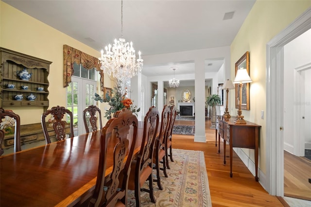 dining room featuring baseboards, an inviting chandelier, a fireplace, and light wood finished floors