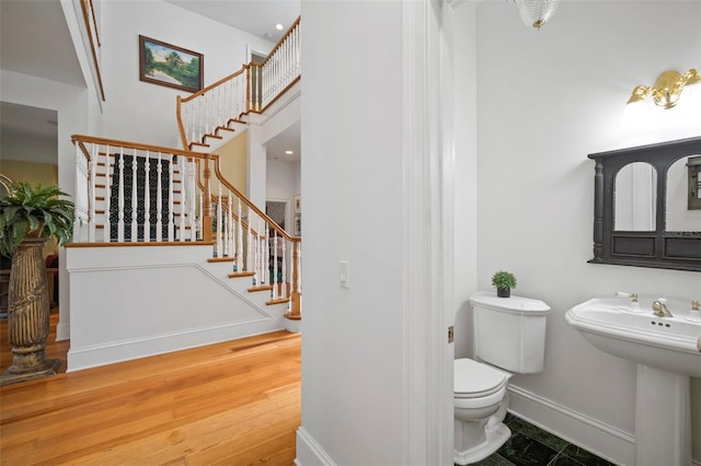 half bathroom featuring a sink, toilet, baseboards, and wood finished floors