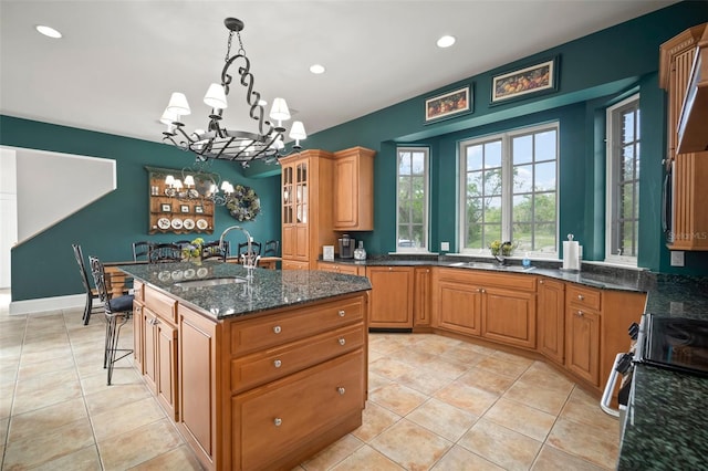 kitchen with a center island with sink, dark stone counters, a breakfast bar area, hanging light fixtures, and a sink