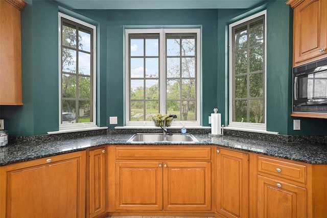 kitchen featuring brown cabinets, dark stone counters, black microwave, and a sink